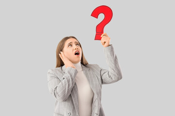 Puzzled businesswoman holding question mark on grey background