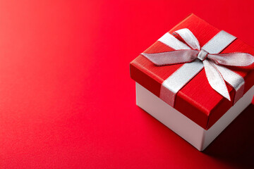 Fototapeta premium Red and white gift box with silver ribbon on red background.