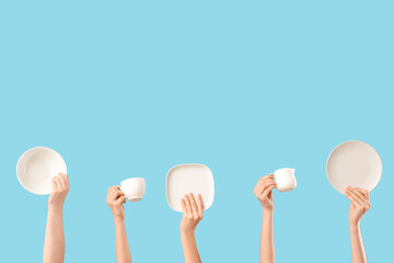 Female hands with plates, bowl, jug and cup on blue background
