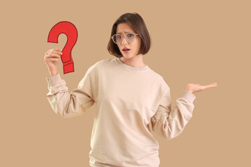 Shocked young woman with paper question mark on beige background