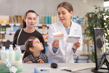 Qualified female pharmacist helps with the choice of medicines and vitamins for a mother with her...