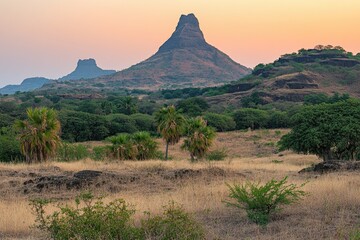 Fototapeta premium Sunrise vista over a dry, hilly landscape with a prominent peak Lush greenery contrasts with the arid terrain