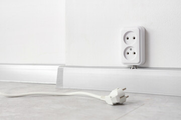 Plug near socket on light wall in room