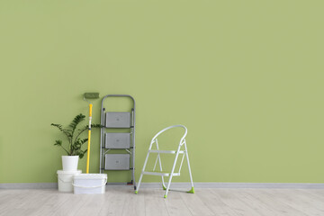 Stepladders with paint roller, buckets and plant near green wall