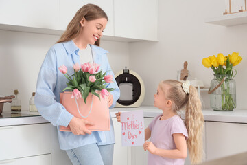 Cute little girl greeting her mom for Mother's Day with tulips and postcard in kitchen © Pixel-Shot