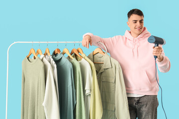 Young man with steamer and clothes on hanger against blue background