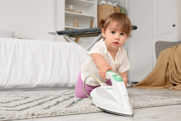 Cute little girl with electric iron on carpet in bedroom. Child at risk