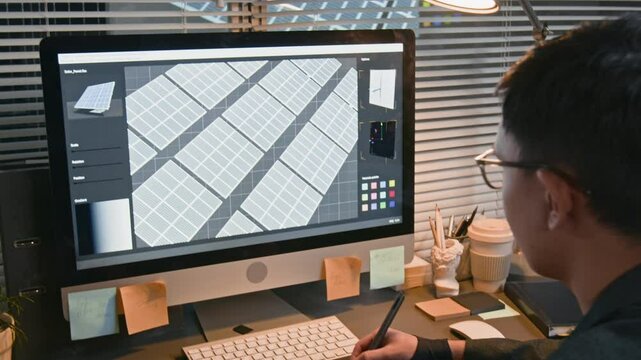 Over shoulder shot of male renewable solutions developer in glasses looking at computer monitor while engineering digital solar power system model using graphic tablet in modern office