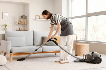 Female janitor vacuum cleaning carpet under sofa at home