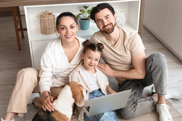 Cute little girl with her parents and Beagle dog using laptop on floor in kitchen
