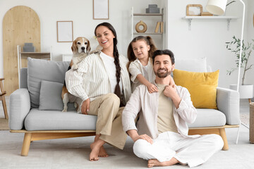 Cute little girl with her parents and Beagle dog sitting on sofa at home