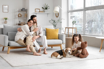 Happy parents hugging while their little daughter playing with toy bear and Beagle dog at home