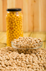 Glass jar with boiled chickpeas and bowl of raw chickpea grains on wooden surface. High quality photo