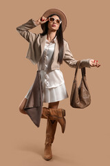 Stylish young woman in sunglasses with bag on brown background
