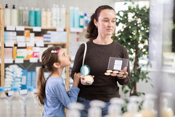 Adult woman with daughter buyers choosing cosmetics for makeup in pharmacy