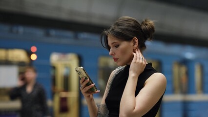 Stylish young woman reading a text message on her mobile phone while waiting for a subway train
