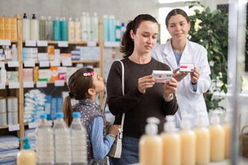 Woman with a child buys paracetamol, reads the instructions on the package and consults with a...