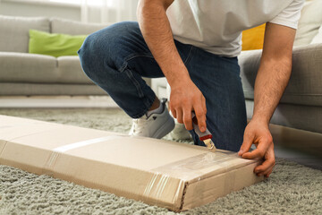 Young man opening box with furniture at home, closeup