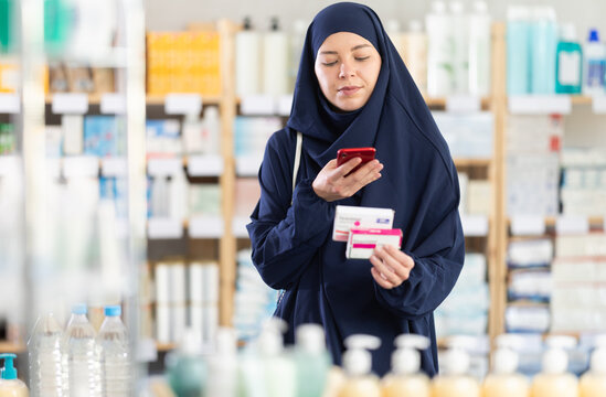 Young woman buyer in hijab scanning qr code for box of paracetamol tablets in pharmacy