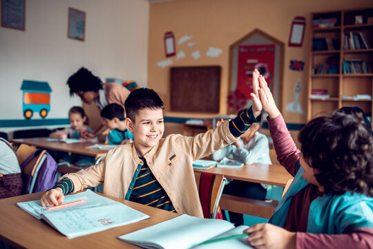 Happy school kids high fiving in classroom after finishing assignment