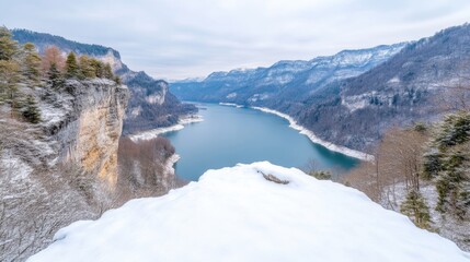 Obraz premium Snowy mountain vista overlooking a serene lake. A dramatic winter landscape with a frozen lake, snow-capped peaks, and rocky cliff faces