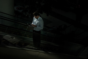 Man, escalator and tablet in night office, global stock market and monitor trading economy online. Business, mockup space and electric stairs in workplace, financial site and email deadline to client