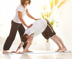 Female yoga instructor training a man to do downward dog pose during a fitness class in an exercise...
