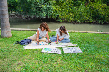 Mother and daughter creating environmental awareness posters in a park