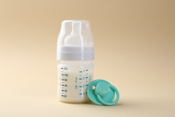 Feeding bottle with milk and pacifier on beige background