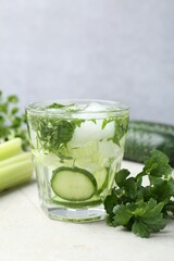 Healthy drink with parsley, cucumbers and celery on light table, closeup