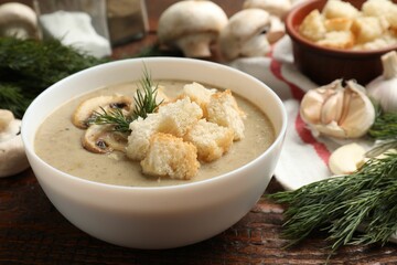 Delicious mushroom cream soup with croutons, dill and ingredients on wooden table, closeup