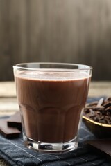 Tasty chocolate milk with shavings and pieces on wooden table, closeup