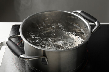 Cooking pot with boiling water and stove on white table against grey background, closeup