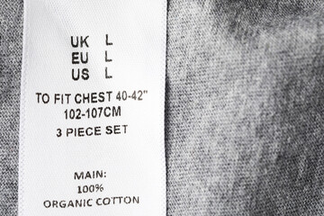 Clothing label with size and content information on grey garment, above view. Space for text