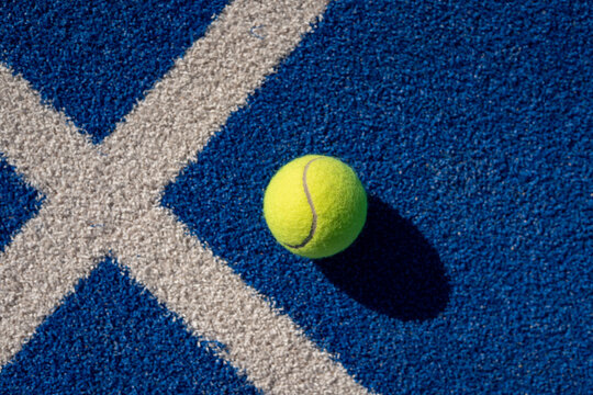 Top view of yellow padel ball on textured blue court with white intersecting lines and shadow - Powered by Adobe