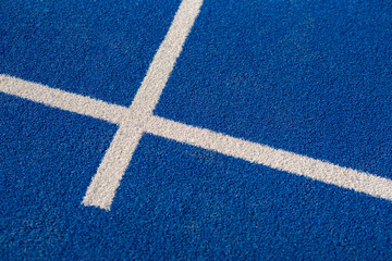 Close-up of white painted lines on blue synthetic surface of padel or tennis court under sunlight, showing texture and geometry