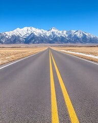Asphalt road vanishing into snow-capped mountains under a clear blue sky