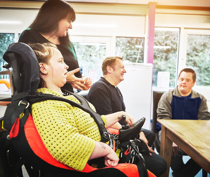 Disability group support meeting with disabled people with handicap in therapy, inclusive and special conversation. Communication, inclusion and young woman in electrical wheelchair in daycare room