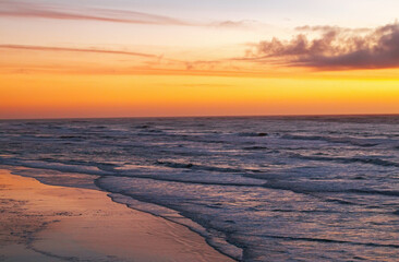 Sunset over the ocean creating a vibrant sky and reflective shoreline