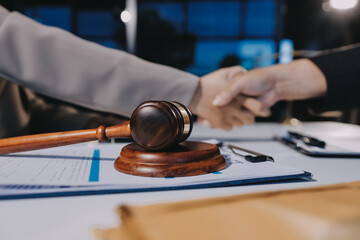 Two businesspeople are shaking hands in a law office with a scale and a gavel on the table.