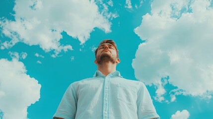 Young man gazing at a vibrant blue sky filled with soft white clouds on a bright sunny day in an outdoor setting