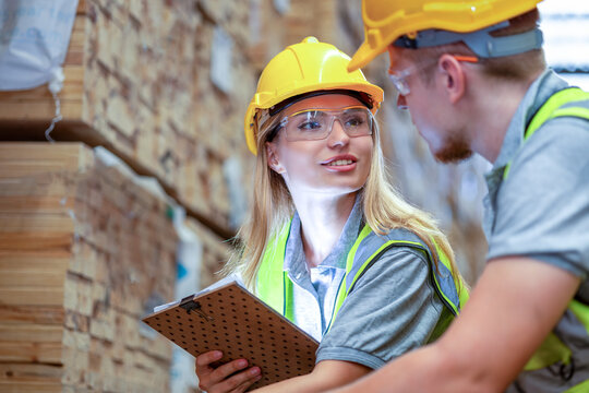 Team engineer carpenter wearing safety uniform and hard hat working holding clipboard checking quality of wooden products at workshop manufacturing. man and woman worker wood warehouse industry.