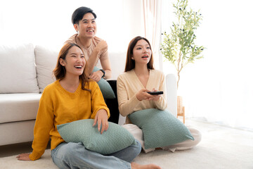 Obraz premium Group young asian friends watching TV together in a cozy living room at home with happy, laughing and enjoying sitting on sofa for watching television with relax, lifestyle and entertainment.