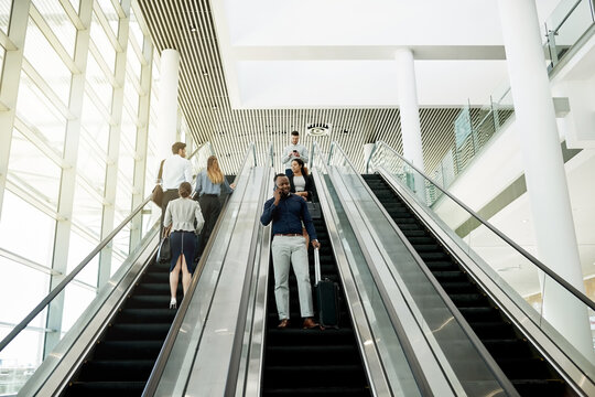 Business, man or luggage with phone call on escalator for meeting schedule, flight information or global networking. Professional, people or travel in lobby with communication, online booking or trip