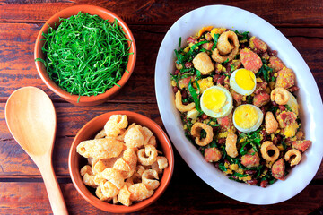 Feijao Tropeiro typical dish of Brazilian cuisine, made with beans, bacon, sausage, collard greens, eggs, on rustic wooden table.
