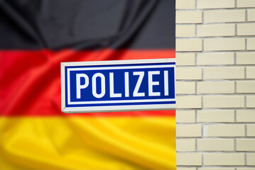 Schild einer Polizeiwache und deutsche Flagge im Hintergrund