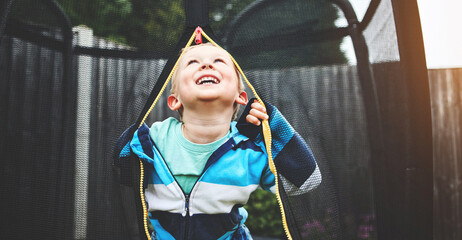 Obraz premium Carefree, playful and happy little boy having fun, playing and enjoying a trampoline in a backyard garden at home. Smiling, innocent and young child looking thoughtful and thinking of game ideas