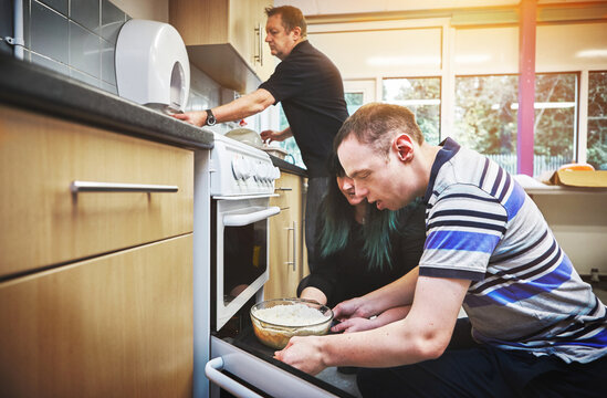 Food, development and disability by man learning basic baking skills in healthcare facility for people with special needs. Mature couple helping male with down syndrome, encourage independence skill