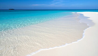 Crystal-clear turquoise water gently laps against a pristine white sandy beach under a bright blue sky.
