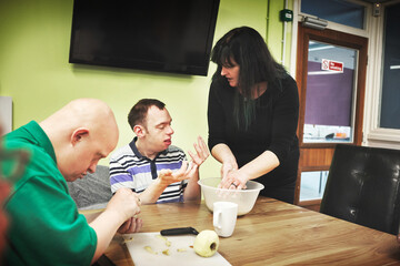 Down syndrome, therapist and men with disability learning mobility to cut apples in a special needs...